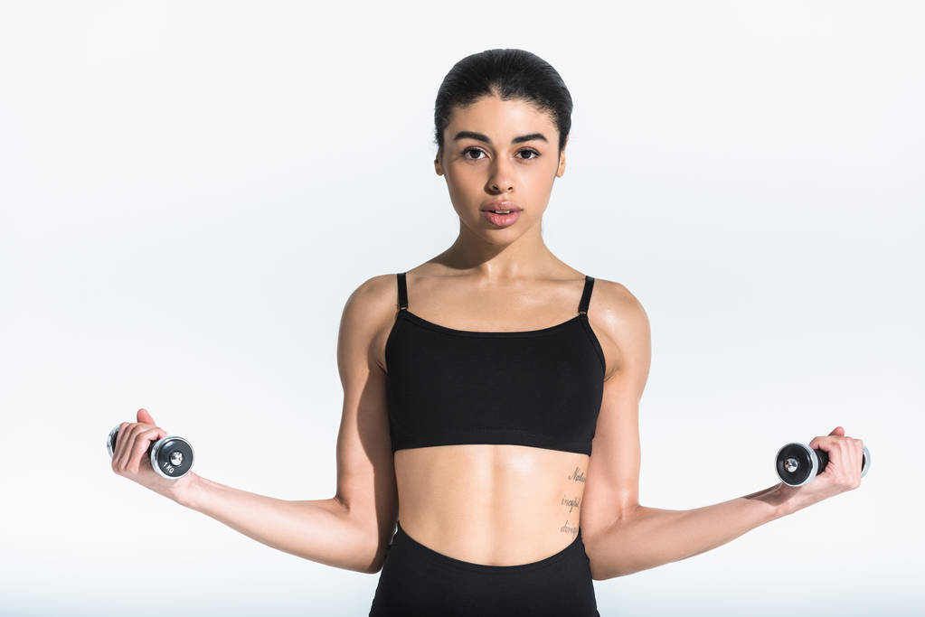 pretty sportive african american girl in black sports bra training with dumbbells on white - Photo, Image