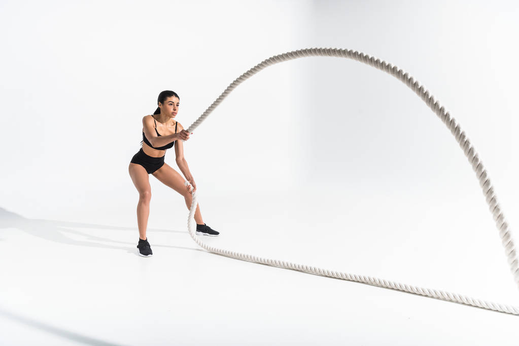 beautiful athletic african american girl training with white ropes on white - Photo, Image