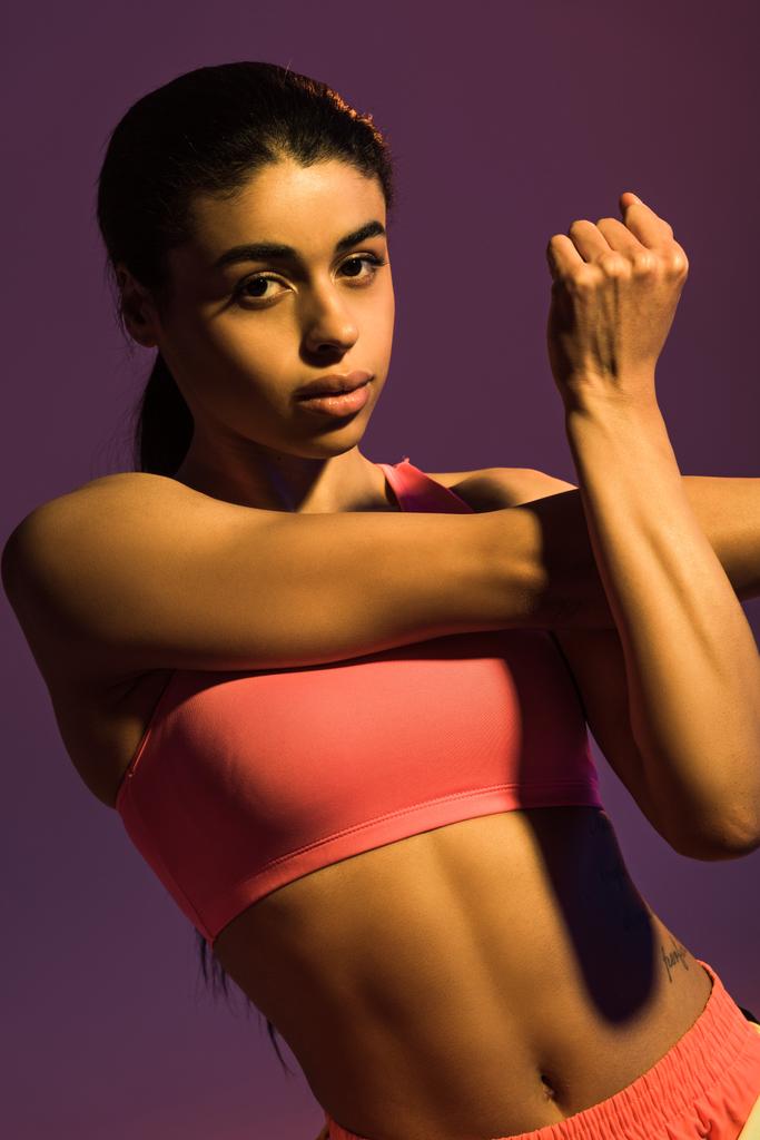 gyönyörű sportív afro-amerikai lány bemelegítés, és nézte a kamerát izolált lila - Fotó, kép