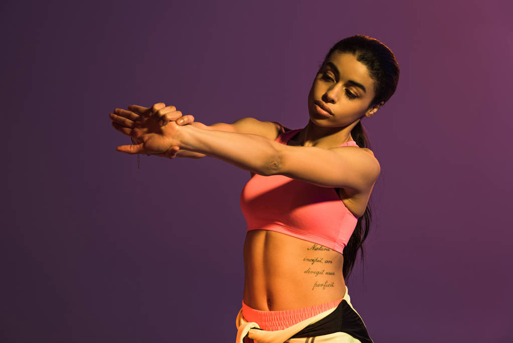 ピンクのスポーツブラジャーでかわいいアフリカ系アメリカ人の女の子は、紫に隔離ウォームアップ - 写真・画像