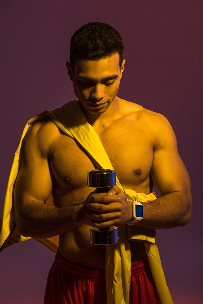 sportive mixed race man with muscular torso holding dumbbell on purple background - Photo, Image