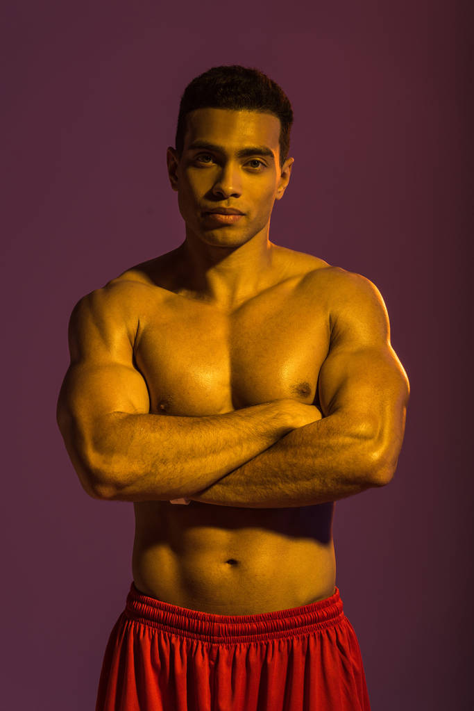 yakışıklı sportif karışık ırk adam mor arka plan üzerinde çapraz kolları ile kamera poz - Fotoğraf, Görsel