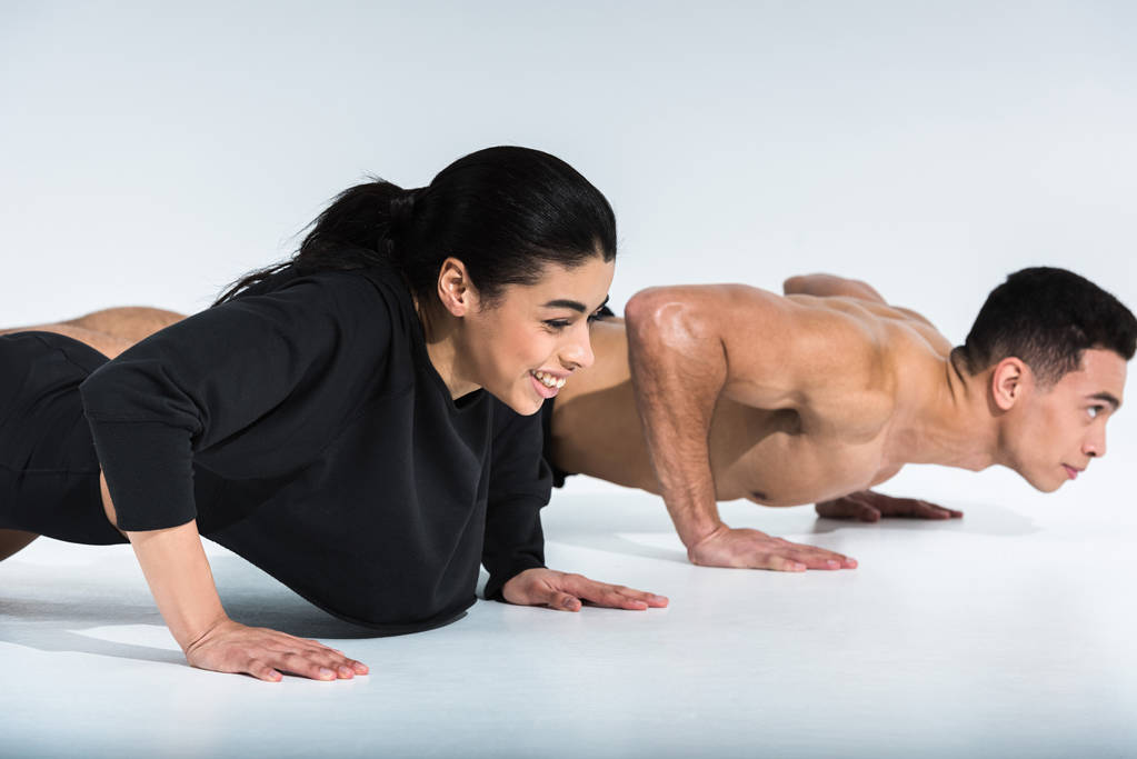 smiling african american girl and mixed race man doing push ups on white - Photo, Image