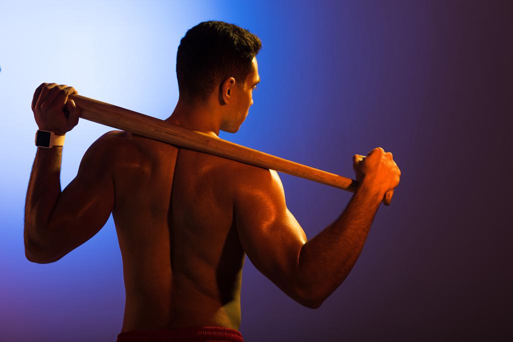 вид сзади спортивного смешанного человека без рубашки с бейсбольной битой на синем и темно-фиолетовом градиентном фоне
 - Фото, изображение
