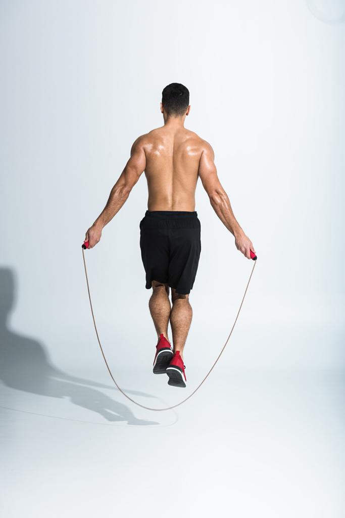 Rückansicht eines athletischen Mannes in schwarzen Shorts, der mit Springseil auf Weiß springt - Foto, Bild