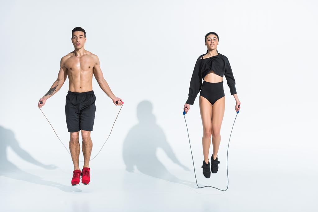 sportliche multikulturelle Frau und Mann springen mit Springseilen auf Weiß - Foto, Bild
