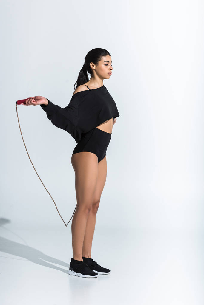 aantrekkelijke Afro-Amerikaanse vrouw in zwarte sportkleding en sneaker training met Jump Rope op wit - Foto, afbeelding