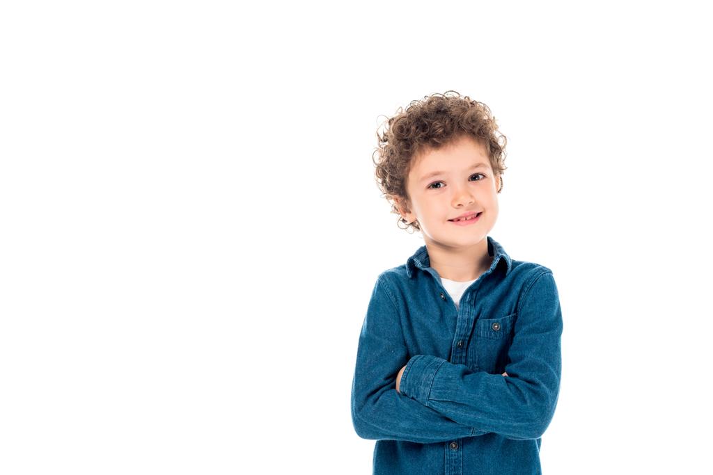 niño rizado sonriente en camisa de mezclilla de pie con brazos cruzados aislados en blanco
 - Foto, imagen