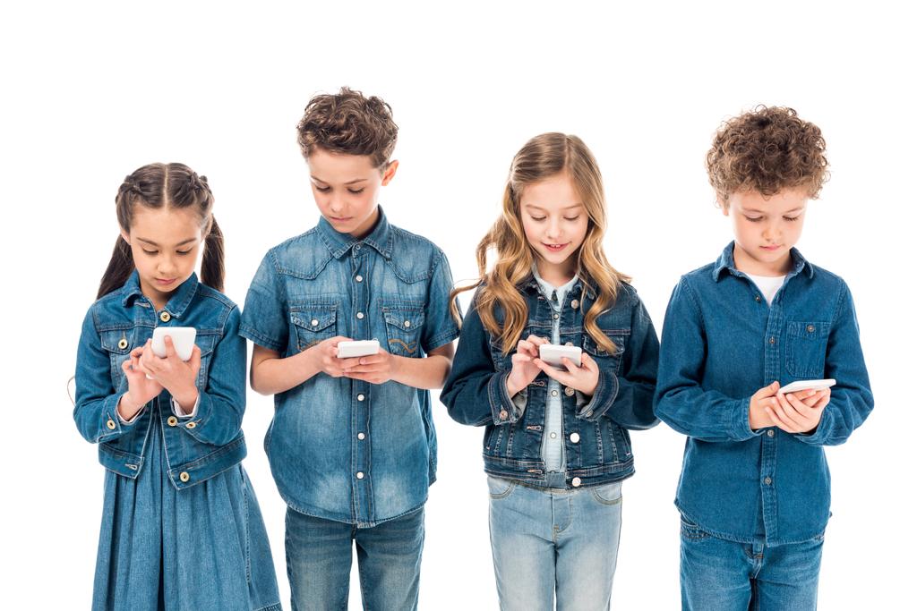 τέσσερα παιδιά σε ρούχα τζιν με χρήση smartphones απομονωμένα σε λευκό - Φωτογραφία, εικόνα