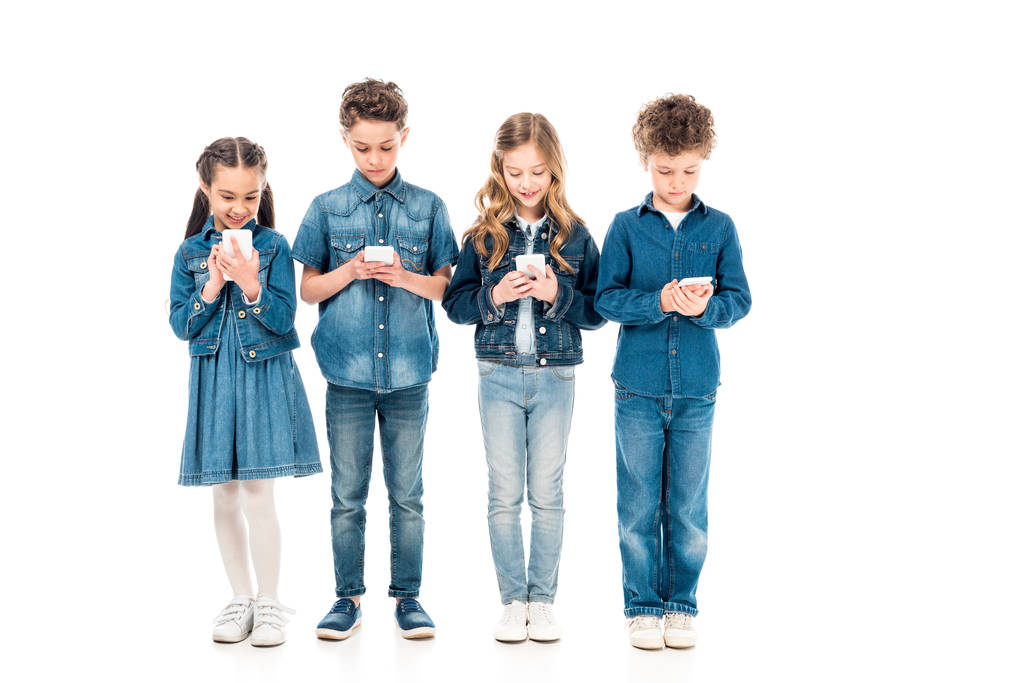 vista a figura intera di quattro bambini in abiti in denim utilizzando smartphone isolati su bianco
 - Foto, immagini