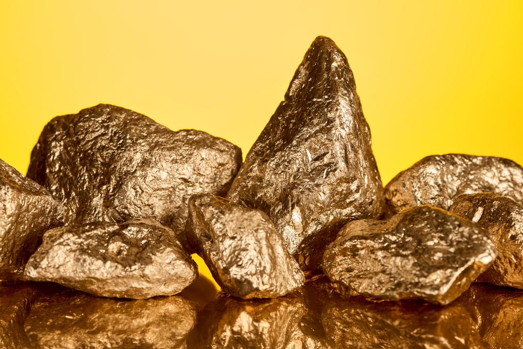 stapel goud glanzende stenen met reflectie geïsoleerd op geel  - Foto, afbeelding