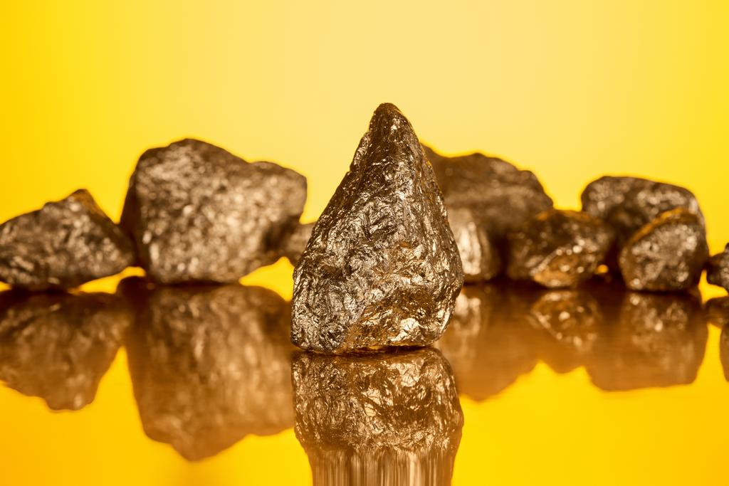selektiver Fokus aus gold glänzendem Stein mit Reflexion isoliert auf gelb  - Foto, Bild