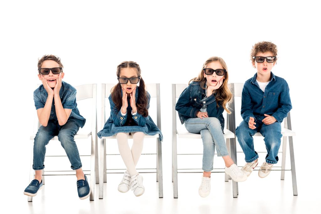 four amazed kids in 3d glasses sitting on chairs on white - Photo, Image