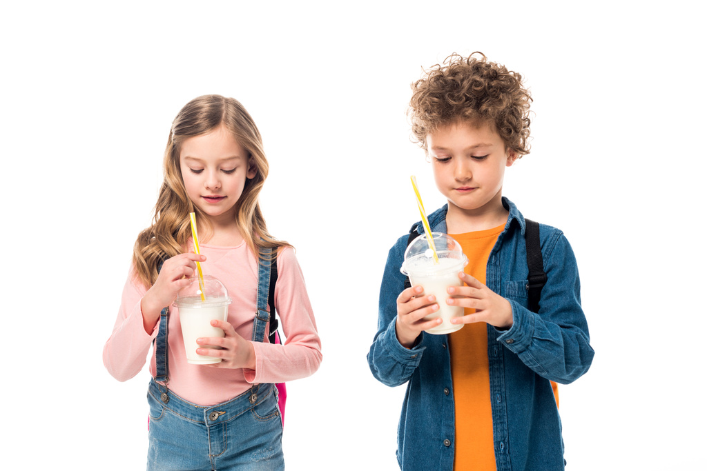 twee schoolkinderen met rugzakken houden milkshakes geïsoleerd op wit - Foto, afbeelding