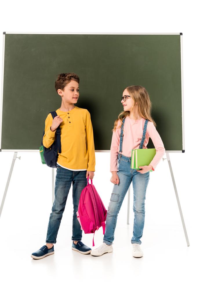 Вид в полный рост двух школьников с рюкзаками, смотрящих друг на друга у доски, изолированной на белом фоне
 - Фото, изображение