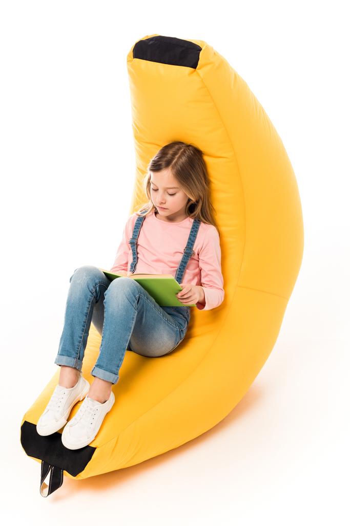 bambino in abiti casual seduto sulla sedia sacchetto di fagioli e libro di lettura su bianco
 - Foto, immagini