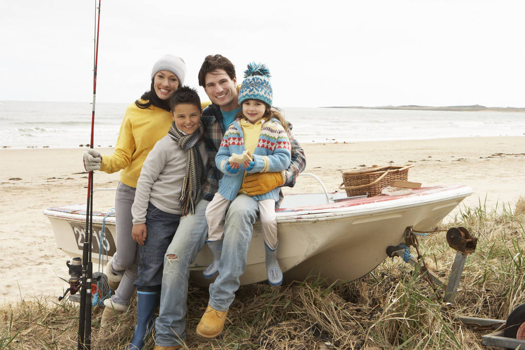 Grupo familiar sentado en barco con caña de pescar en la playa de invierno
 - Foto, Imagen