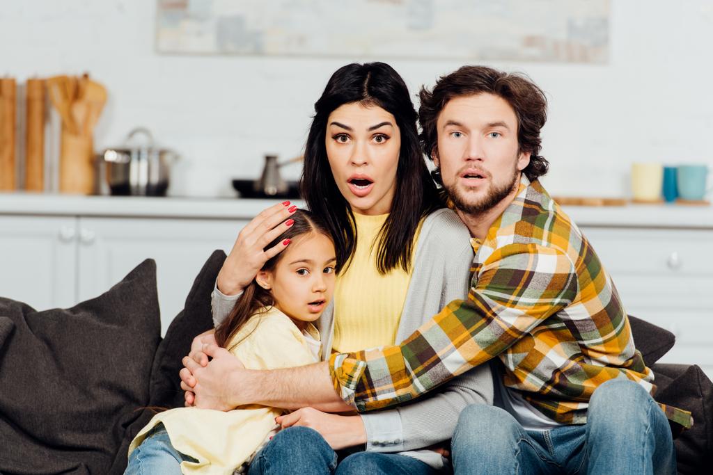 scioccato marito e moglie guardando la tv e abbracciando carina figlia
  - Foto, immagini