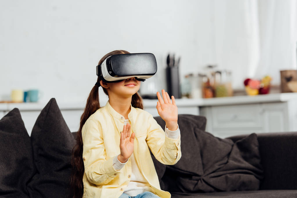 entzückendes Kind gestikuliert, während es Virtual-Reality-Headset zu Hause trägt  - Foto, Bild