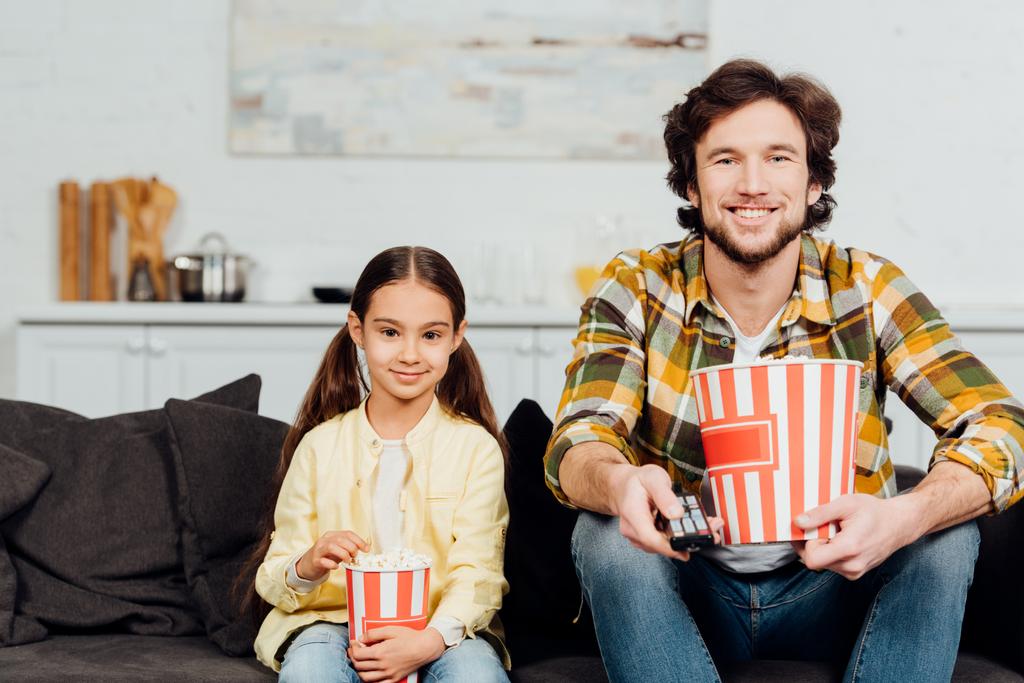 happy father and daughter watching tv and holding popcorn buckets  - Photo, Image
