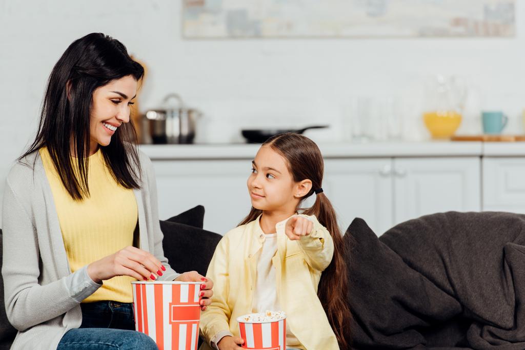 glückliches Kind zeigt mit dem Finger auf Mutter mit Eimer Popcorn  - Foto, Bild