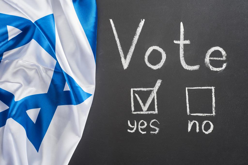 top view of vote lettering and check mark in square near yes word on black chalkboard near flag of Israel - Photo, Image