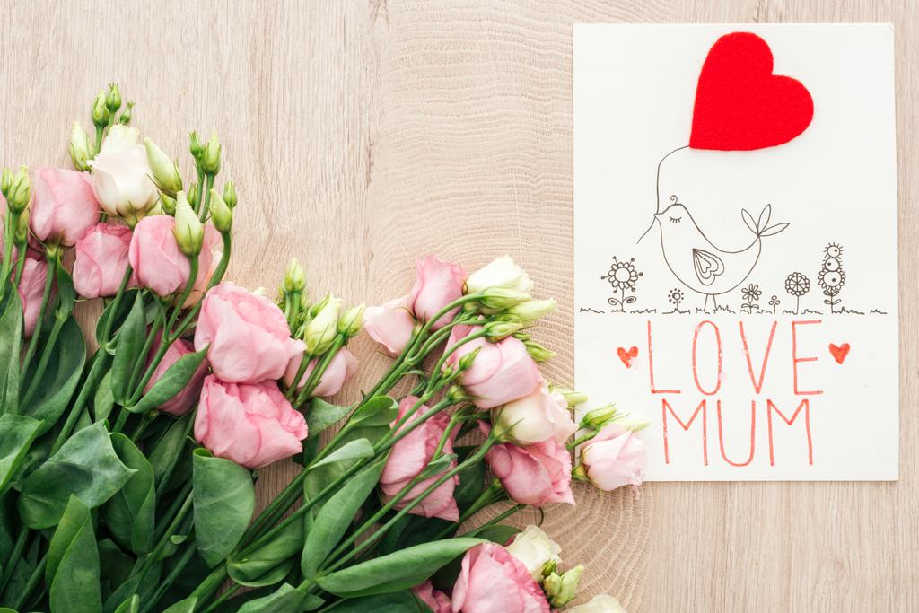 Draufsicht auf rosa Eustoma-Blumen und Karte mit Liebesmama-Worten auf Holztisch - Foto, Bild