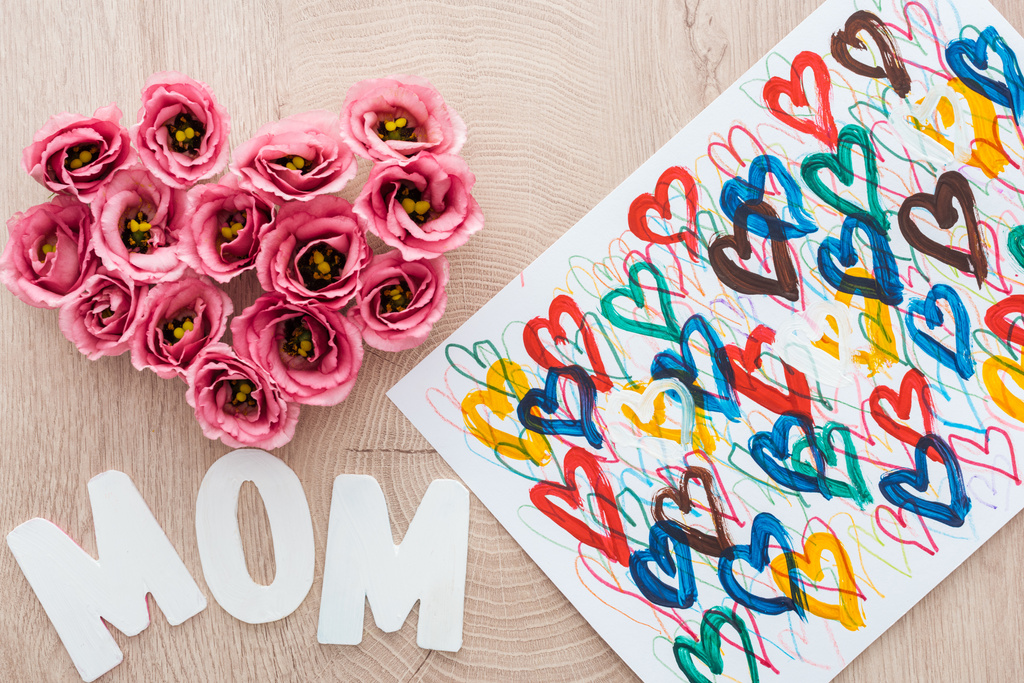 Draufsicht auf Herzschild aus Eustoma-Blumen, Zeichnung und Mutti-Zeichen auf Holztisch - Foto, Bild