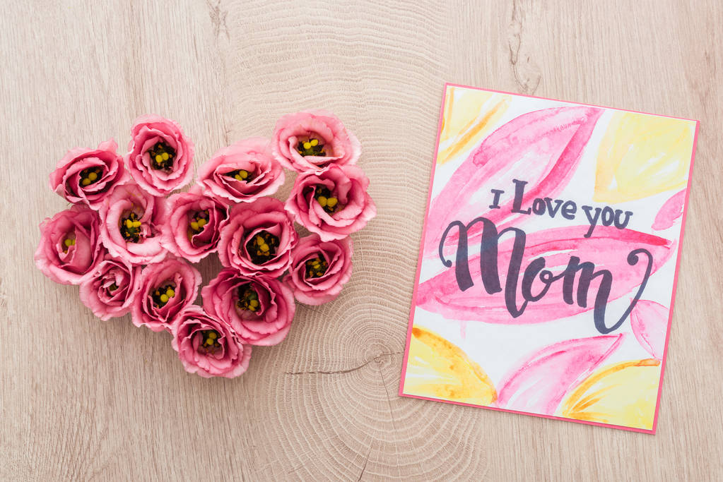top view of heart sign made of eustoma flowers and card with i love you mom lettering on wooden surface - Photo, Image