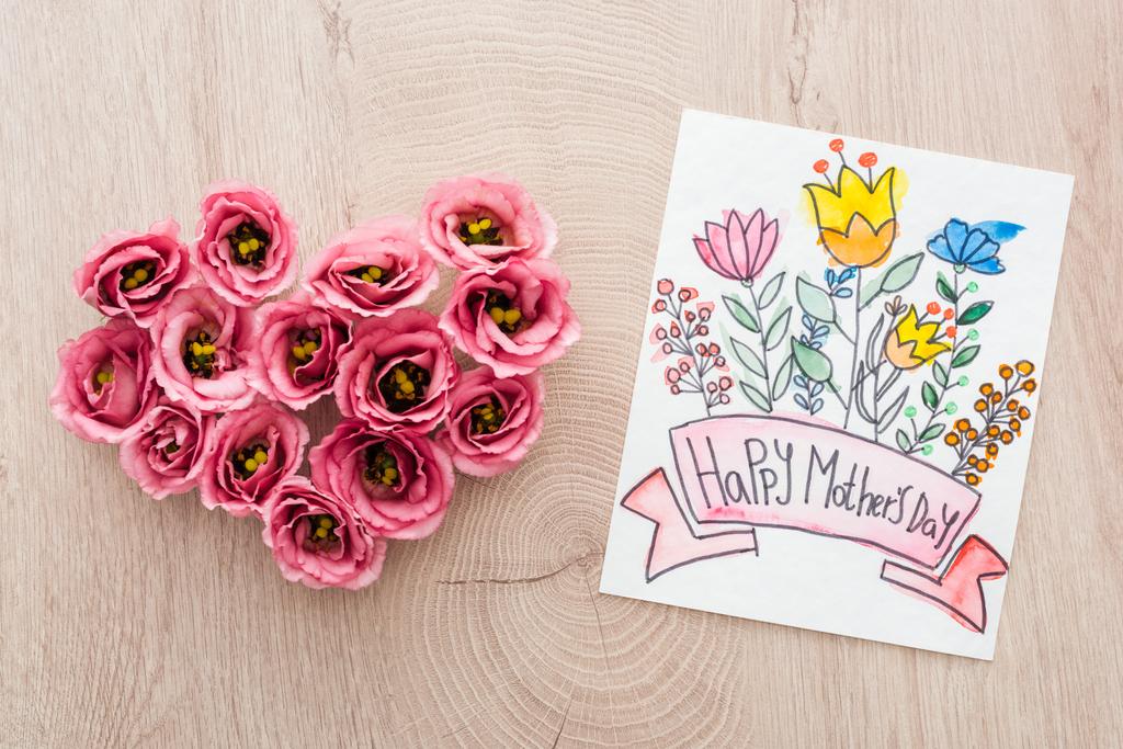 Top uitzicht van hart teken gemaakt van Eustoma bloemen en kaart met Happy Mothers Day schrijven op houten tafel - Foto, afbeelding