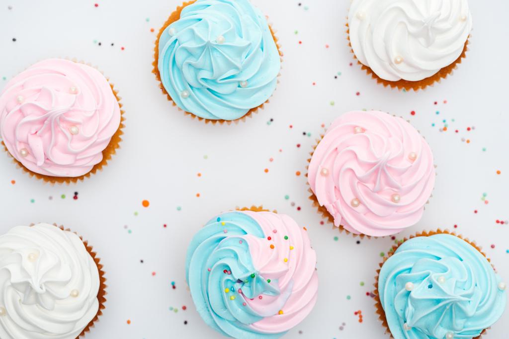vista superior de deliciosos cupcakes blancos, rosados y azules con aspersiones aisladas en blanco
 - Foto, imagen