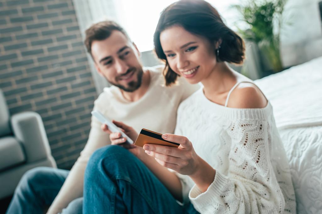 szelektív középpontjában a boldog nő gazdaság okostelefon, és nézi a hitelkártya közelében vidám ember  - Fotó, kép
