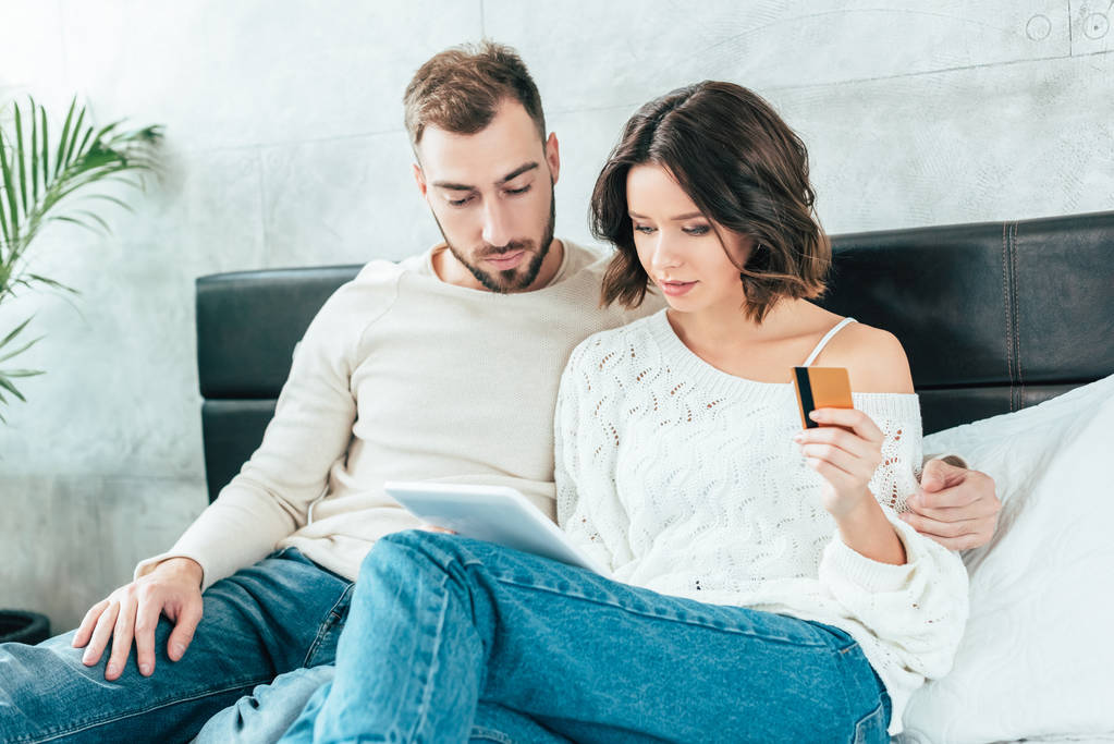 hombre guapo mirando tableta digital cerca atractiva mujer sosteniendo tarjeta de crédito
  - Foto, Imagen