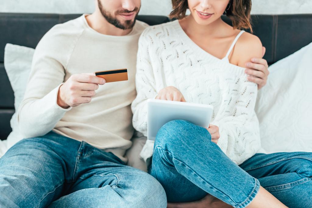 visão cortada de homem segurando cartão de crédito e mulher abraçando com tablet digital
 - Foto, Imagem