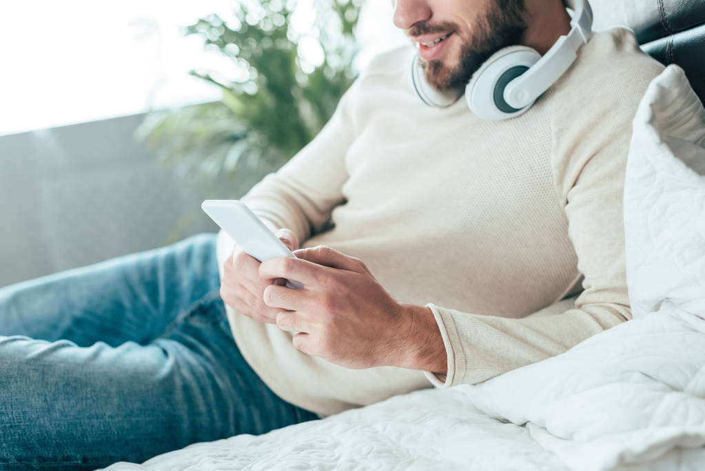 cropped view of cheerful bearded man in headphones holding smartphone at home - Photo, Image