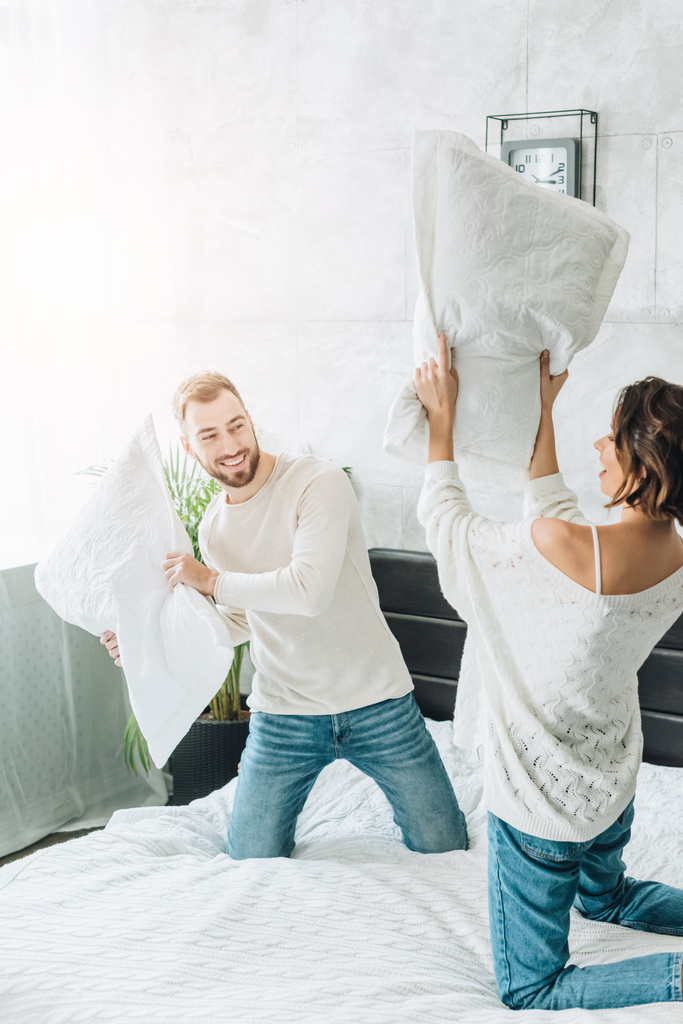 ベッドの上で陽気な女性と枕の戦いを持つ幸せなひげの男  - 写真・画像