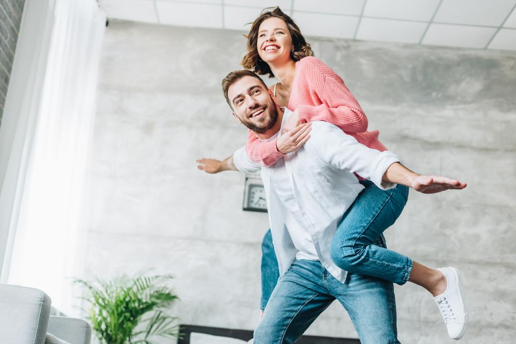 low angle view of happy bearded man piggybacking cheerful brunette woman  - Photo, Image