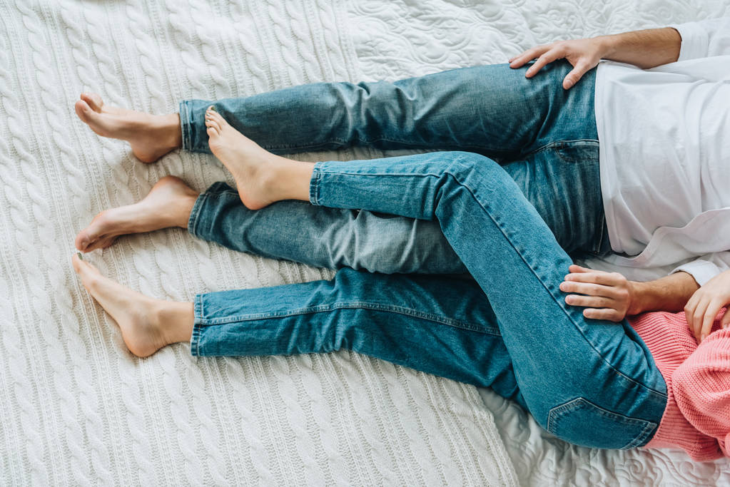 Ausgeschnittene Ansicht von Mann und Frau in Jeans, die auf dem Bett liegen  - Foto, Bild