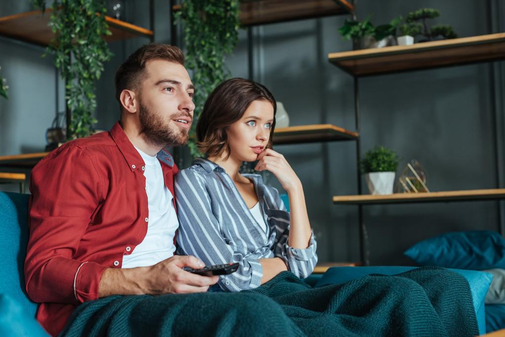 handsome man holding remote controller while watching movie with woman at home  - Photo, Image
