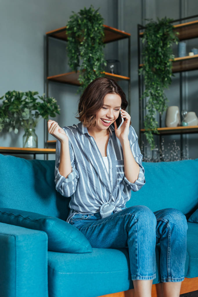 mujer alegre gesto mientras habla en el teléfono inteligente en la sala de estar
  - Foto, imagen