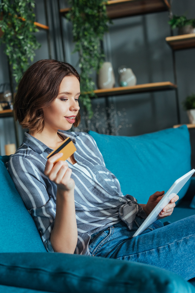 attraktive Frau schaut auf digitales Tablet, während sie Kreditkarte hält  - Foto, Bild