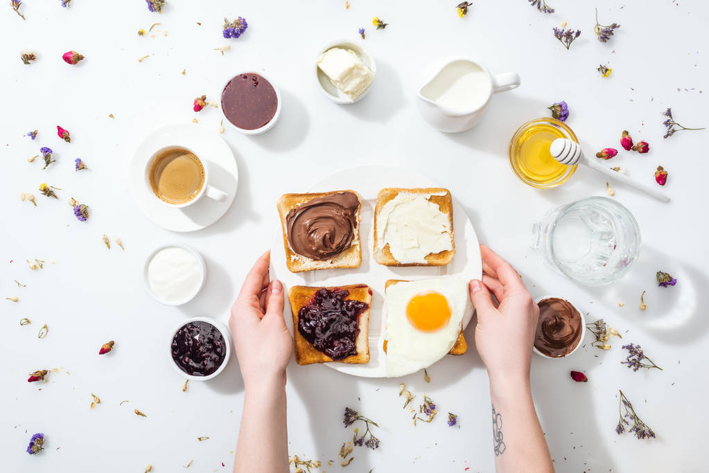 przycięte widok kobiety z tatuażem w ręku trzymając talerz smaczne śniadanie na białym  - Zdjęcie, obraz