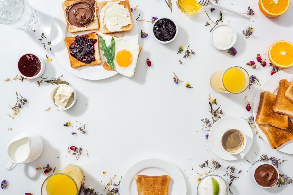 вид сверху на тарелки с вкусными тостами рядом с напитками и мисками с вареньем на белом
  - Фото, изображение