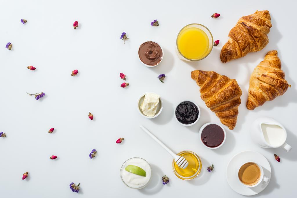 vista dall'alto di gustosi croissant vicino a ciotole con marmellata, succo d'arancia e fiori secchi su bianco
  - Foto, immagini