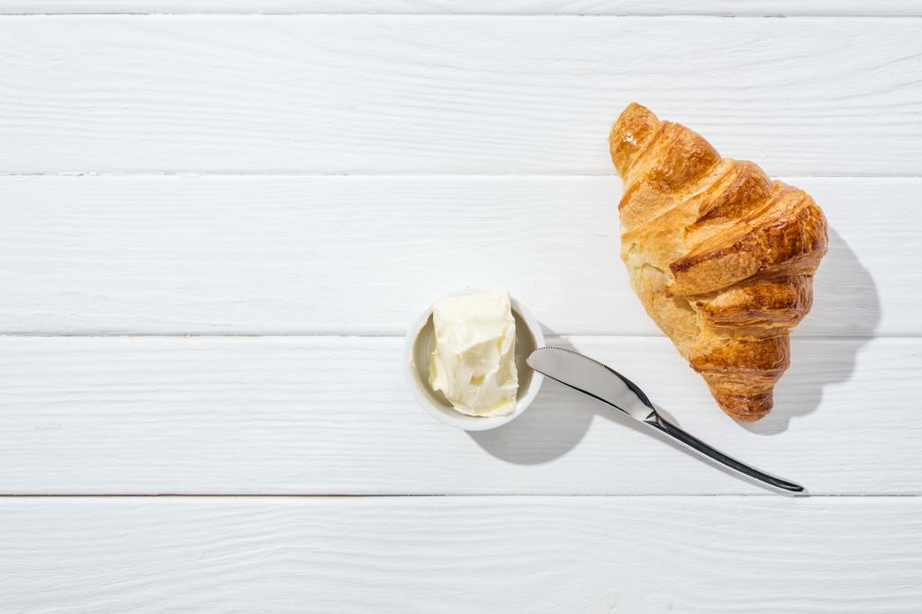 pohled na nůž v blízkosti mísy se smetanovým sýrem a croissant na bílém   - Fotografie, Obrázek