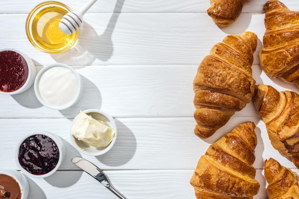 felülnézet friss croissant közeli tálak krémsajttal, csokoládé krém, tejföl, dzsem és méz fehér - Fotó, kép