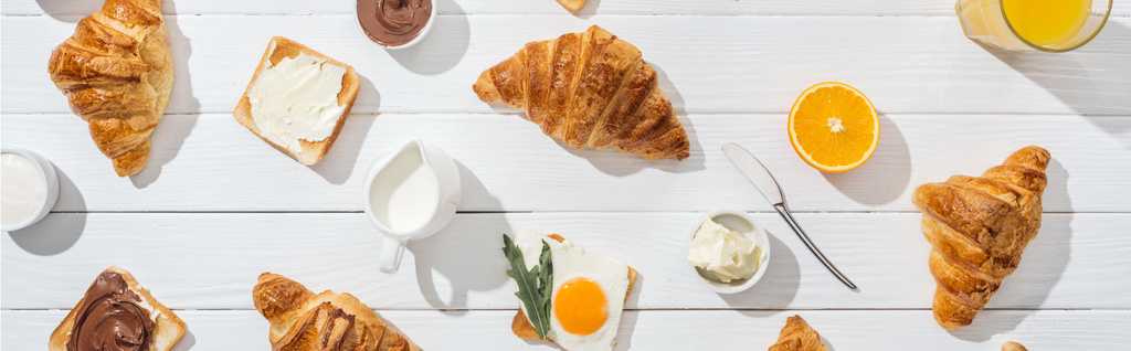 panoramatický záběr sladkých croissantů v blízkosti chutných toastů a nápojů na bílém  - Fotografie, Obrázek