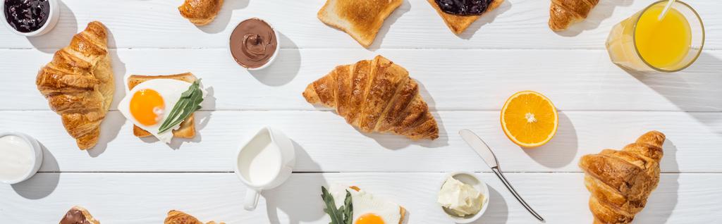 panoramic shot of sweet croissants near tasty toasts with fried eggs on white  - Photo, Image