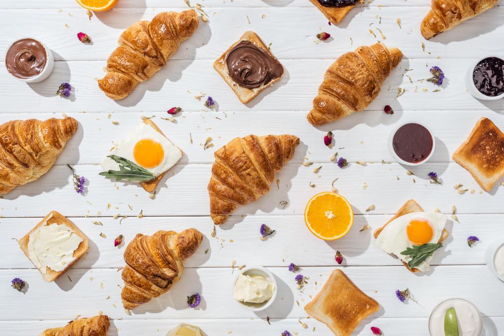 top view of sweet croissants and tasty toasts with fried eggs near dried flowers on white  - Photo, Image