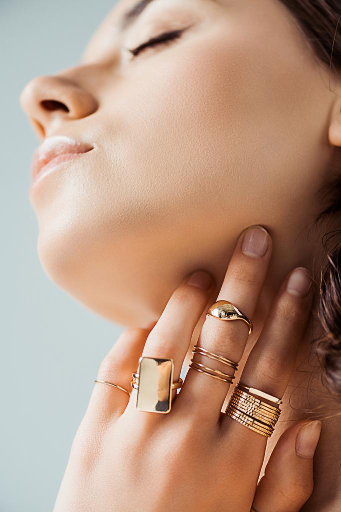 giovane donna in anelli dorati toccando collo isolato su grigio
 - Foto, immagini